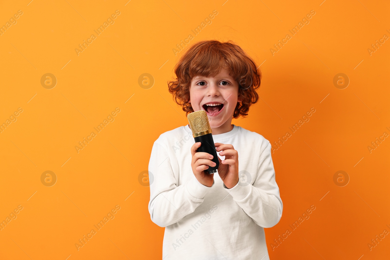 Photo of Little boy with microphone singing on orange background