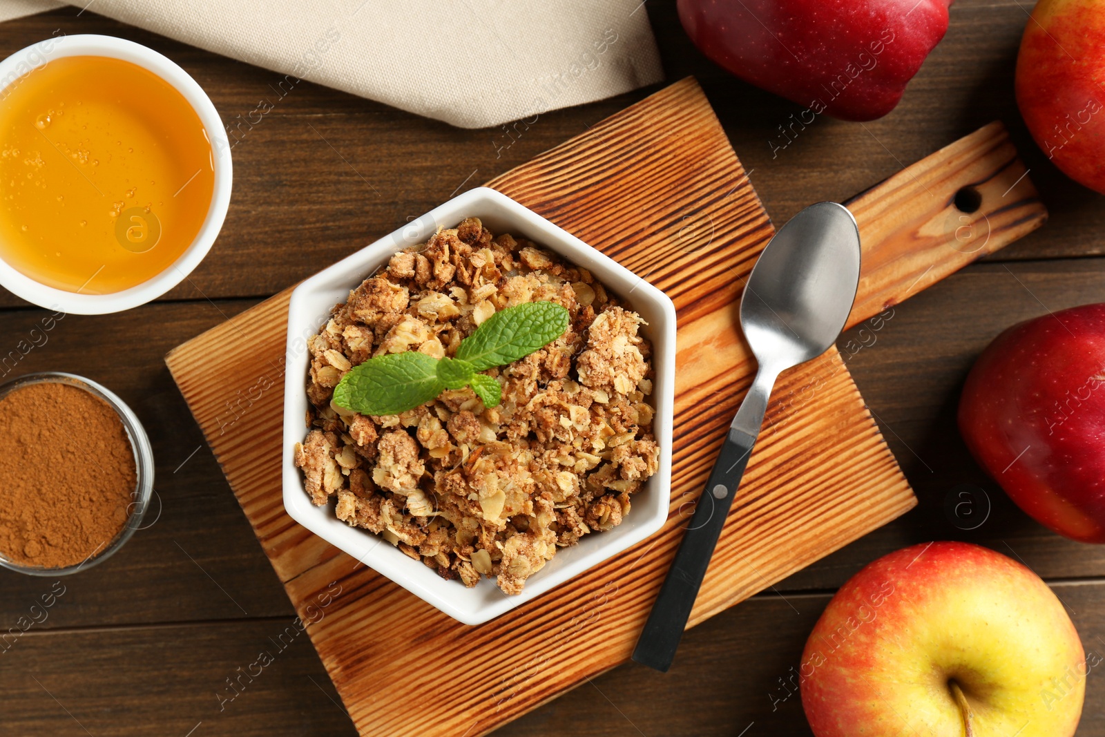 Photo of Tasty apple crisp in bowl, ingredients and spoon on wooden table, flat lay