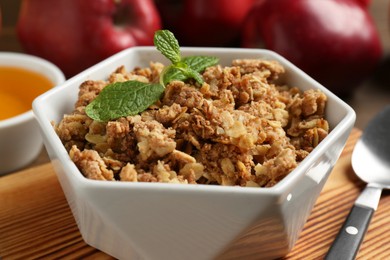 Photo of Tasty apple crisp in bowl, ingredients and spoon on table, closeup