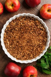 Photo of Tasty apple crisp in baking dish, fresh fruits and mint on wooden table, flat lay