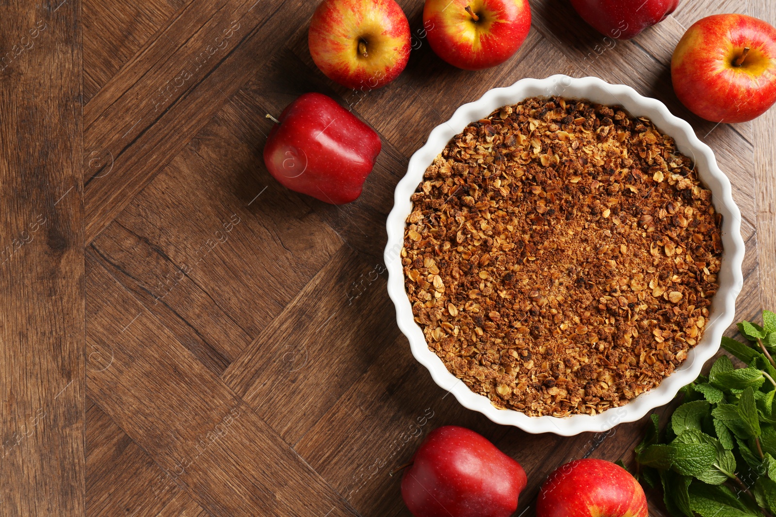 Photo of Tasty apple crisp in baking dish, fresh fruits and mint on wooden table, flat lay. Space for text