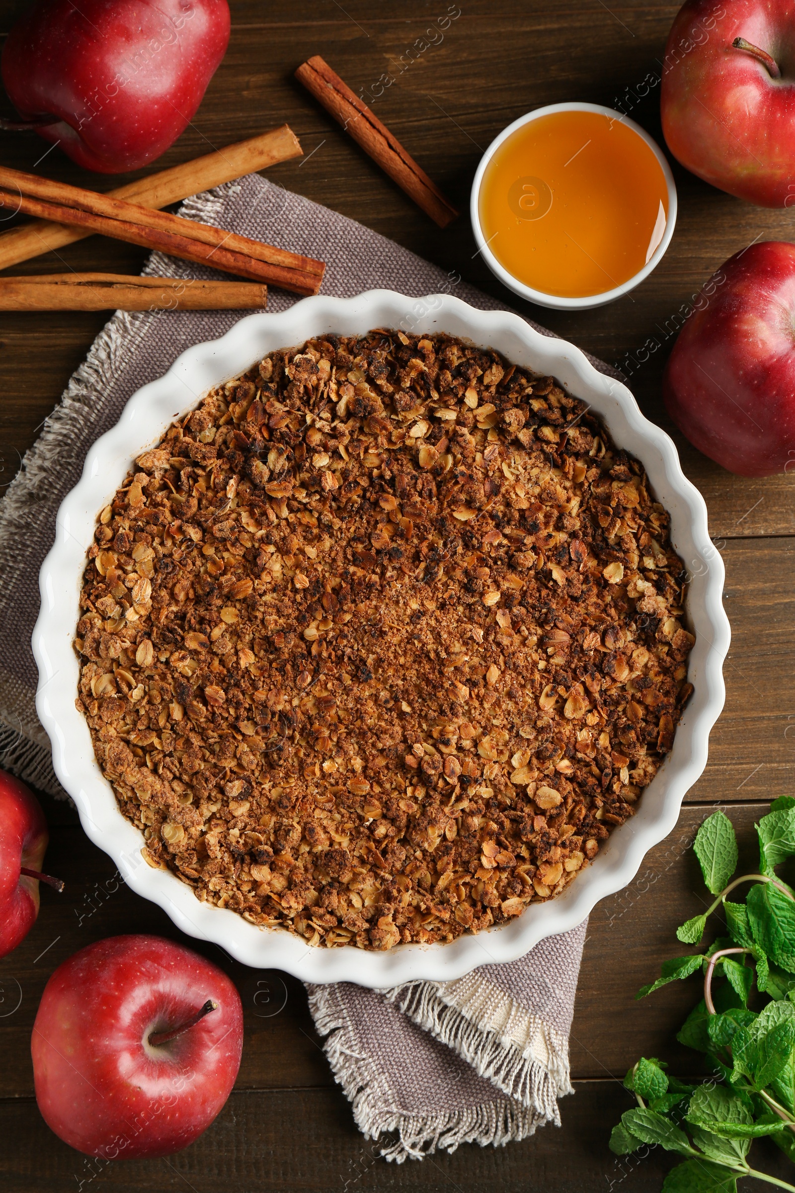 Photo of Tasty apple crisp in baking dish and ingredients on wooden table, flat lay