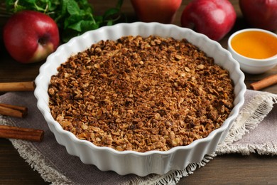 Photo of Tasty apple crisp in baking dish and ingredients on wooden table, closeup