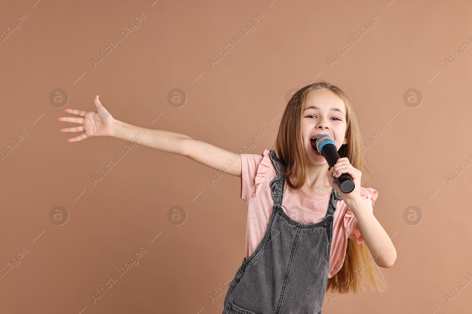 Photo of Little girl with microphone singing on light brown background