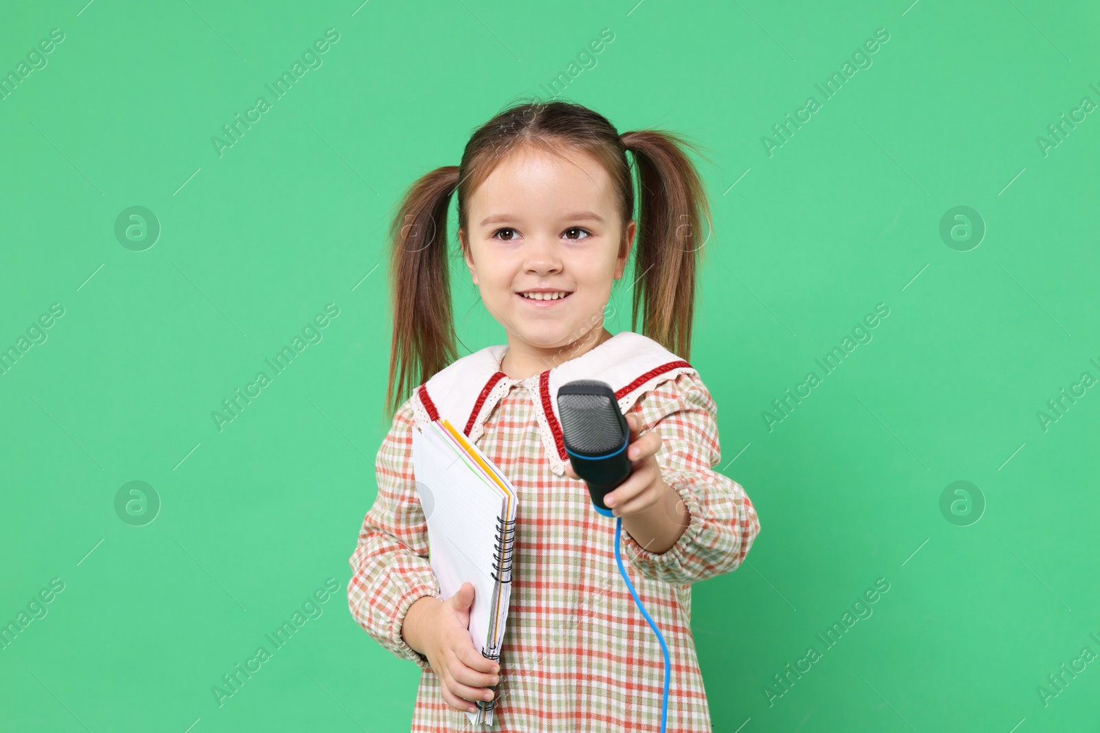 Photo of Smiling girl with microphone and notebook on green background