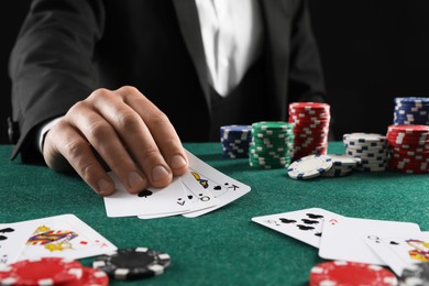 Man with cards and casino chips playing poker at gambling table, closeup