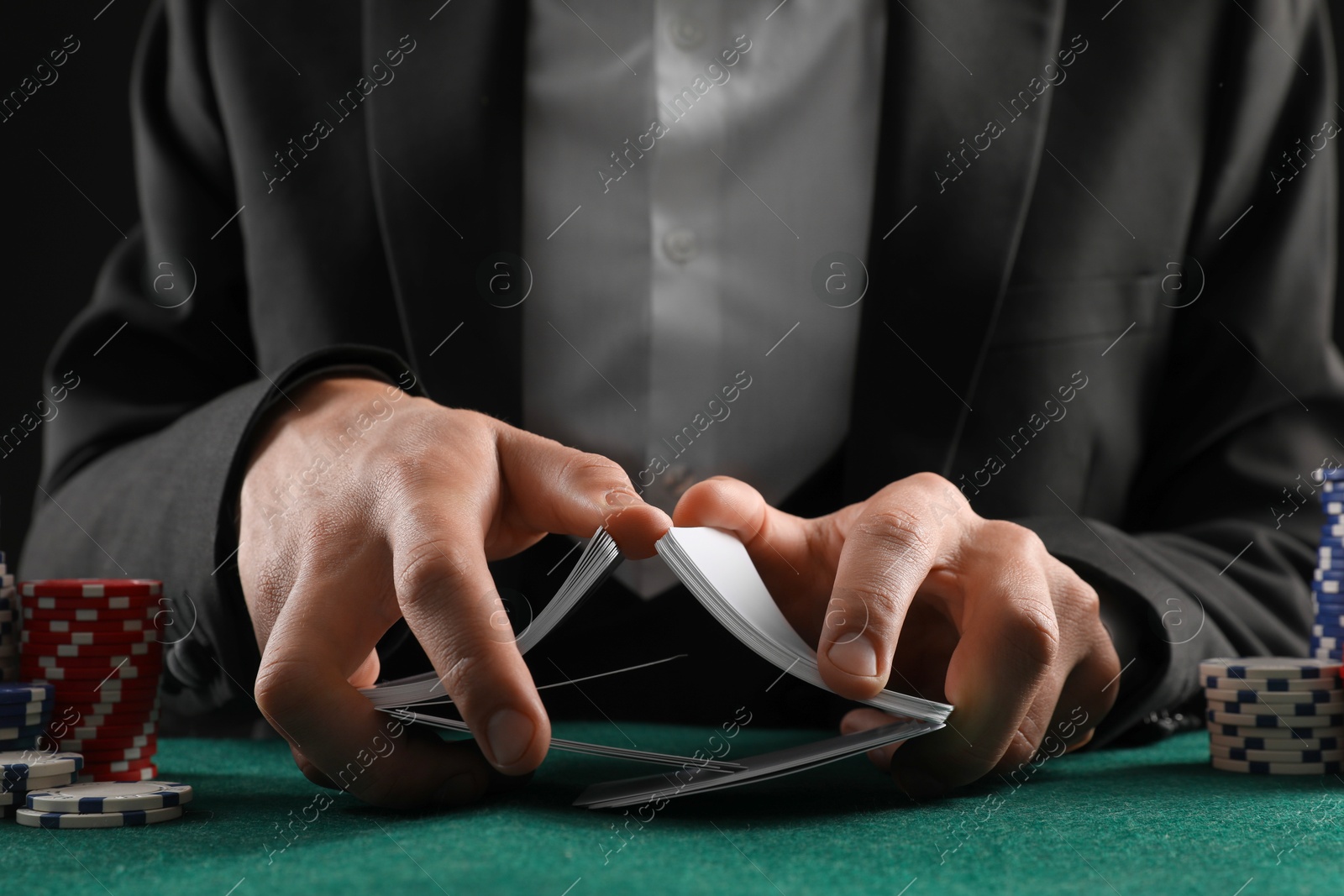 Photo of Man with casino chips shuffling playing cards at gambling table, closeup. Poker concept