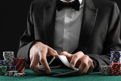 Photo of Man with casino chips shuffling playing cards at gambling table, closeup. Poker concept