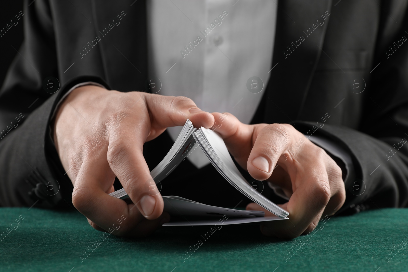 Photo of Man with casino chips shuffling playing cards at gambling table, closeup. Poker concept