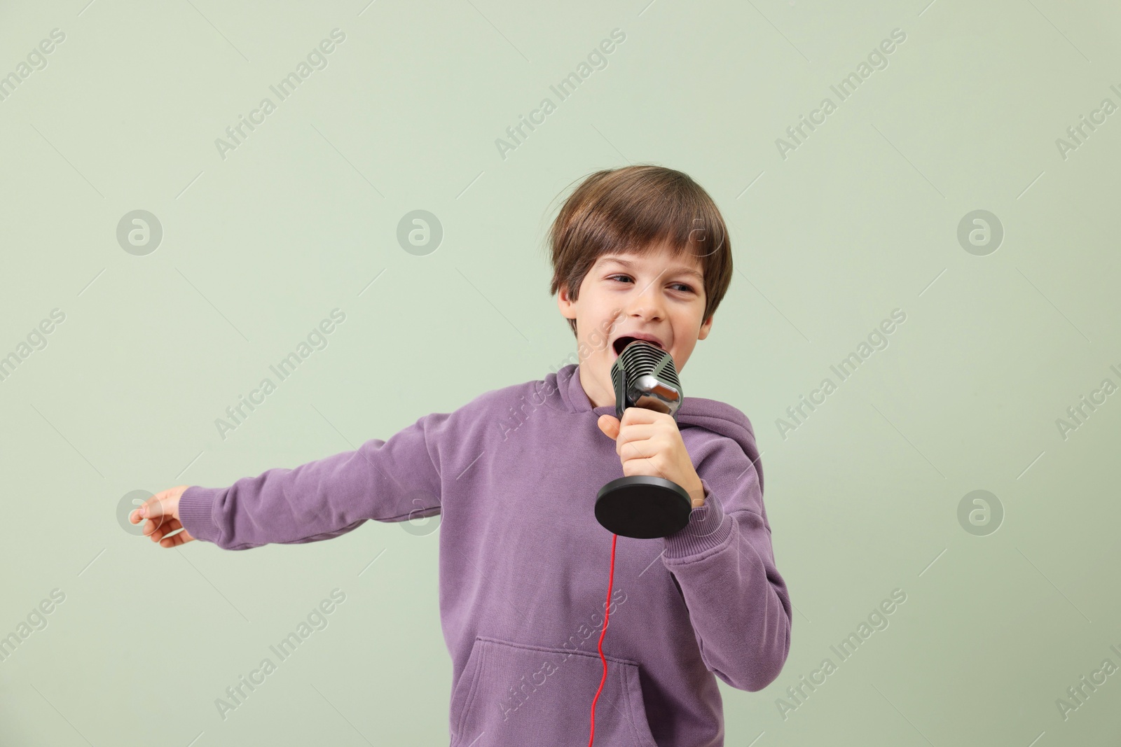 Photo of Cute boy with microphone singing near green wall