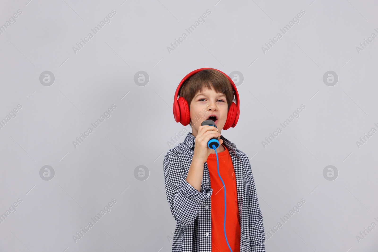 Photo of Cute boy with microphone in headphones singing near grey wall. Space for text