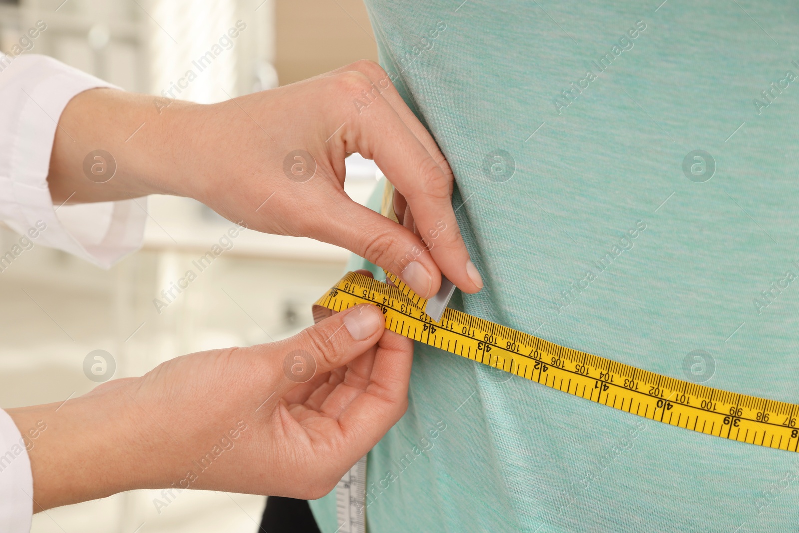 Photo of Nutritionist measuring overweight woman's waist with tape in hospital, closeup