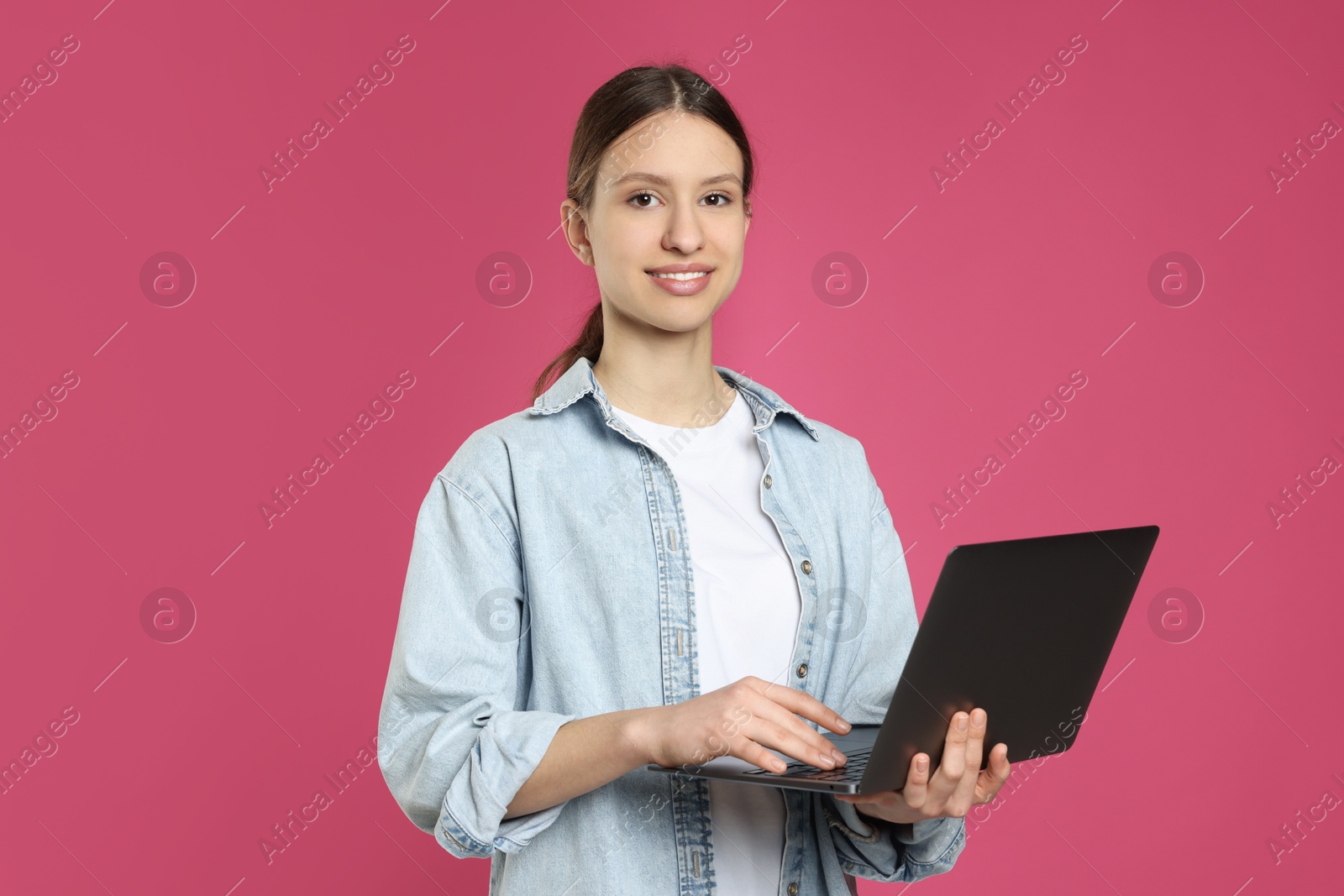 Photo of Portrait of smiling teenage girl with laptop on pink background