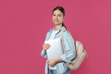 Photo of Portrait of smiling teenage girl with laptop on pink background