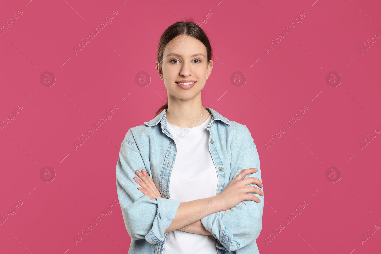 Photo of Portrait of smiling teenage girl with crossed arms on pink background