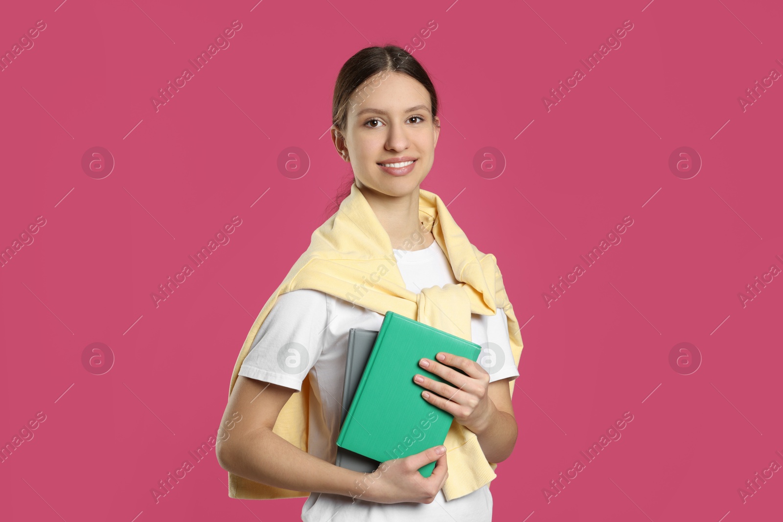 Photo of Portrait of smiling teenage girl with books on pink background