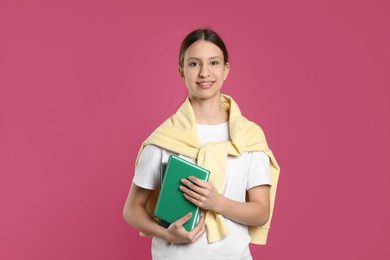 Photo of Portrait of smiling teenage girl with books on pink background