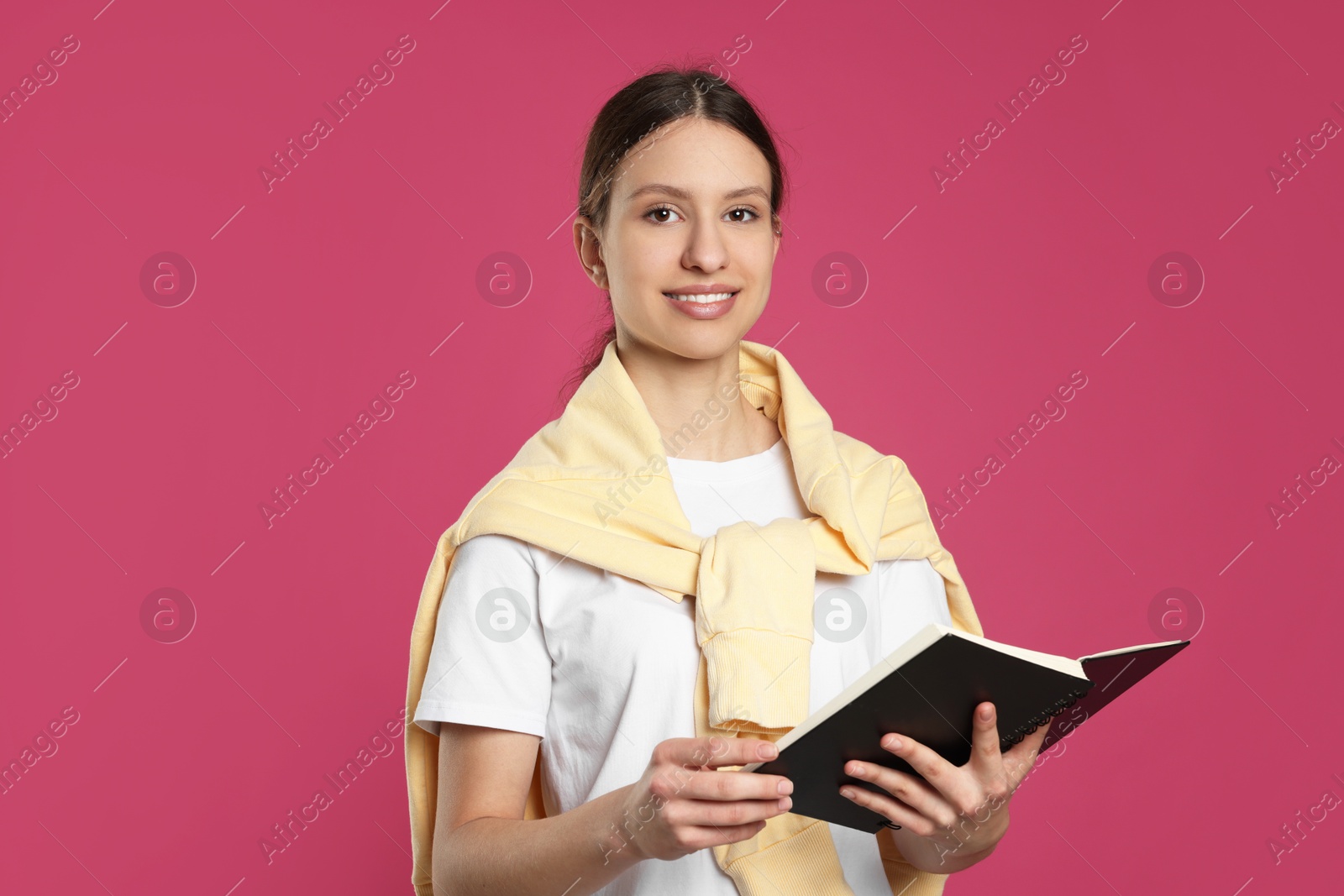 Photo of Portrait of smiling teenage girl with book on pink background