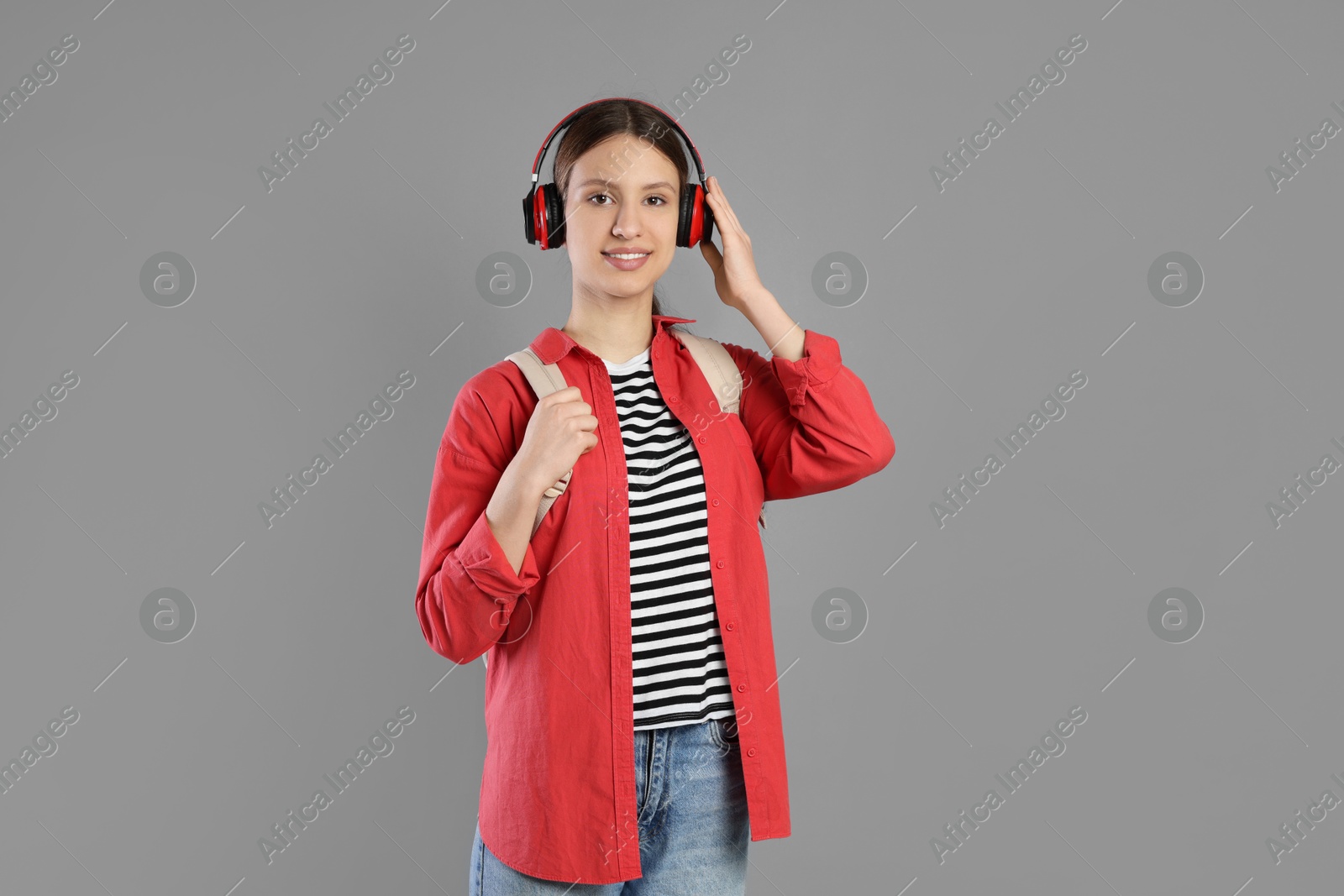 Photo of Portrait of smiling teenage girl in headphones with backpack on grey background