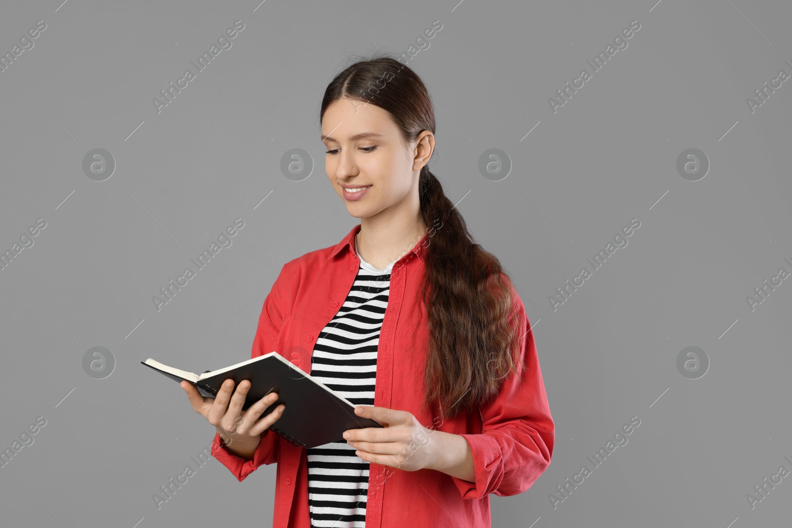 Photo of Portrait of smiling teenage girl reading book on grey background