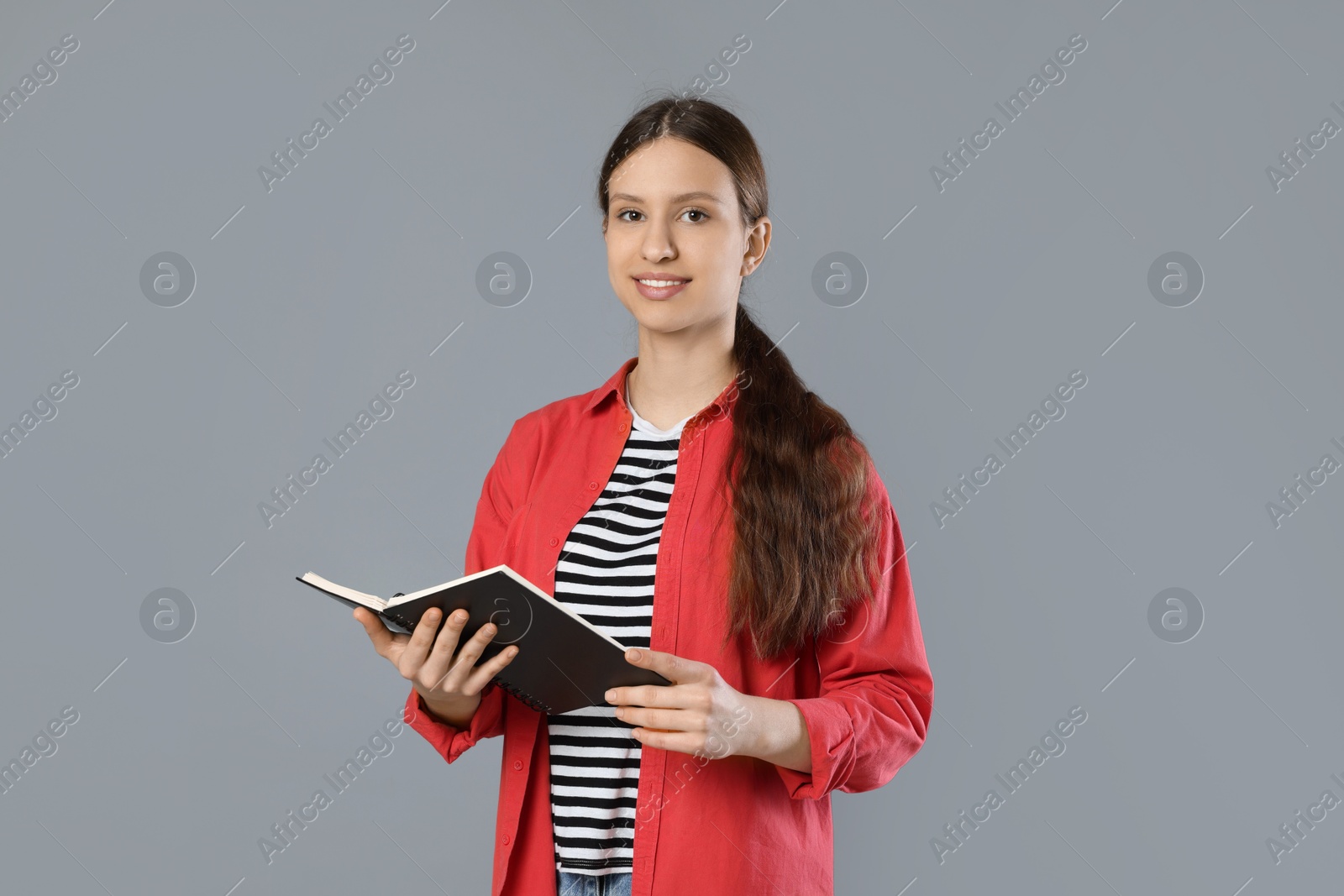 Photo of Portrait of smiling teenage girl with book on grey background