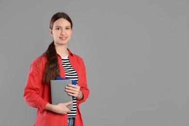 Photo of Portrait of smiling teenage girl with books on grey background. Space for text