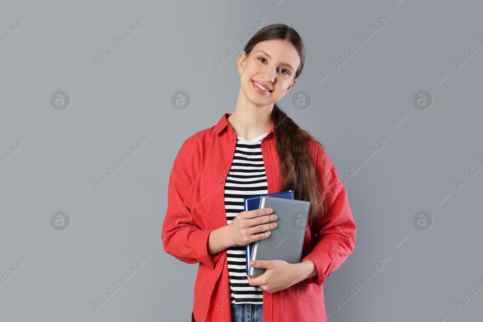 Photo of Portrait of smiling teenage girl with books on grey background