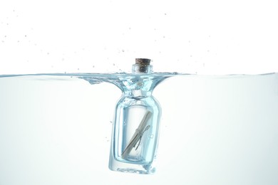 Photo of Corked glass bottle with rolled letter in water on white background