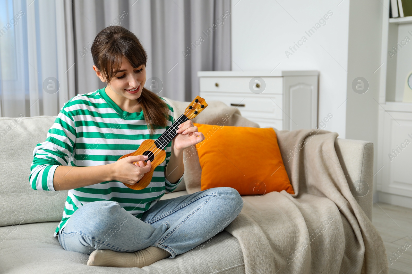 Photo of Happy woman playing ukulele on sofa at home