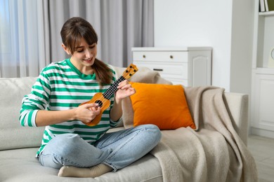 Photo of Happy woman playing ukulele on sofa at home