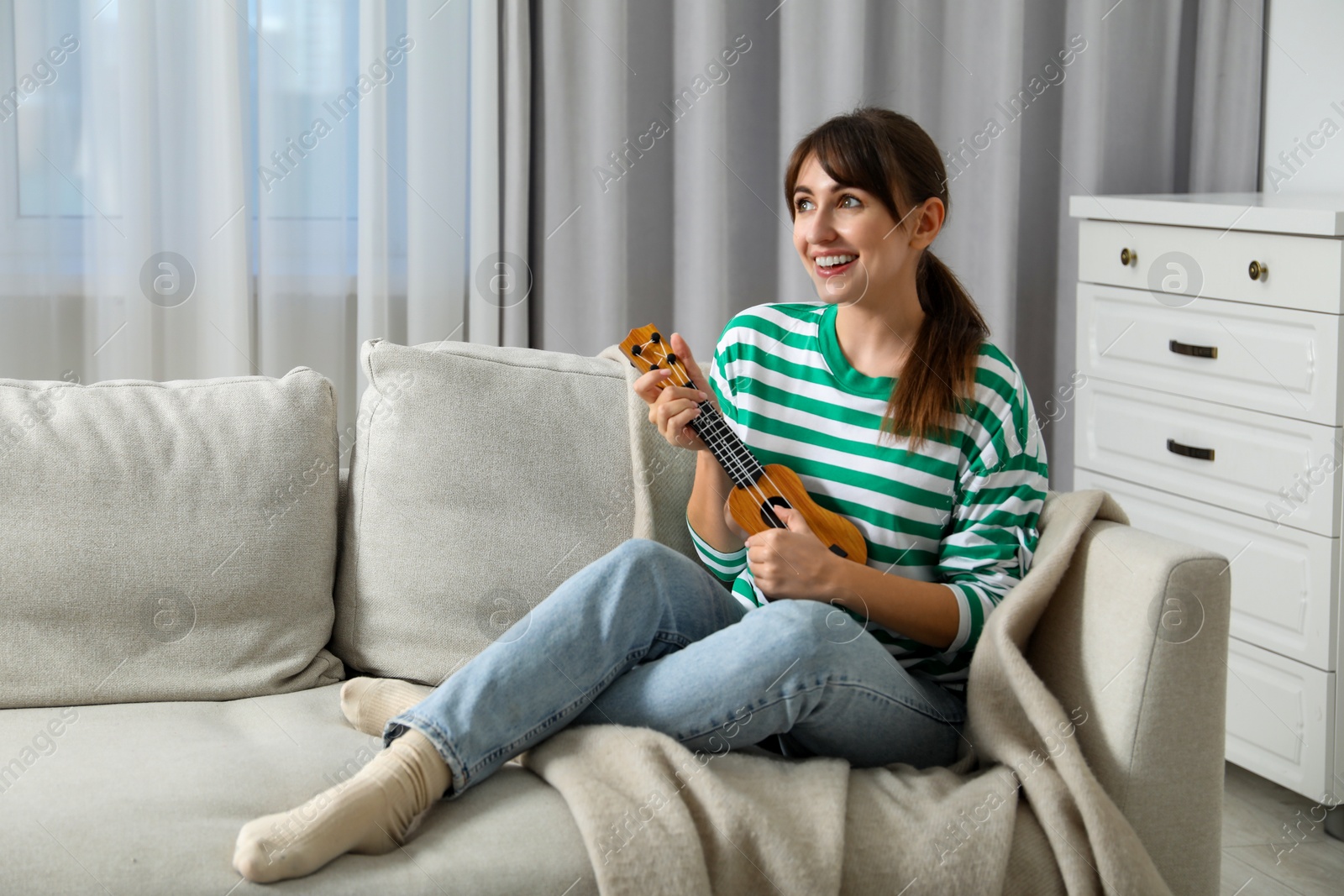 Photo of Happy woman playing ukulele on sofa at home