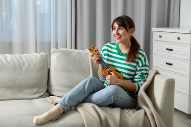 Photo of Happy woman playing ukulele on sofa at home