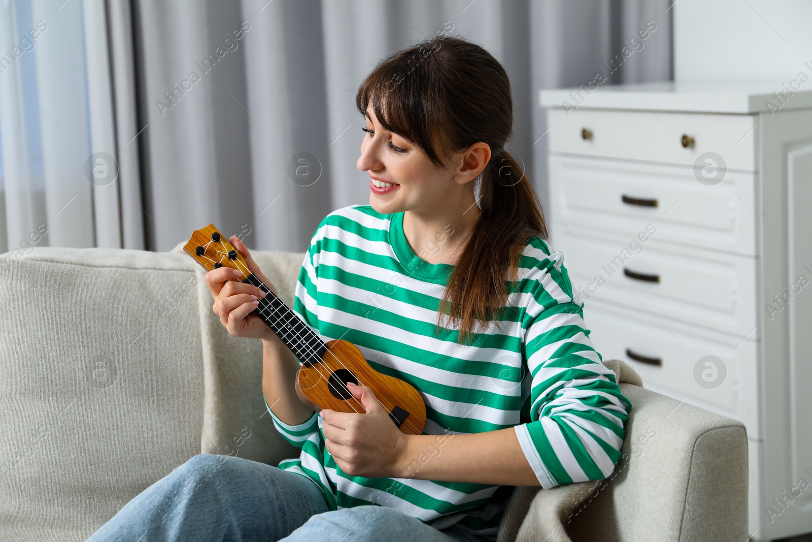 Photo of Happy woman playing ukulele on sofa at home