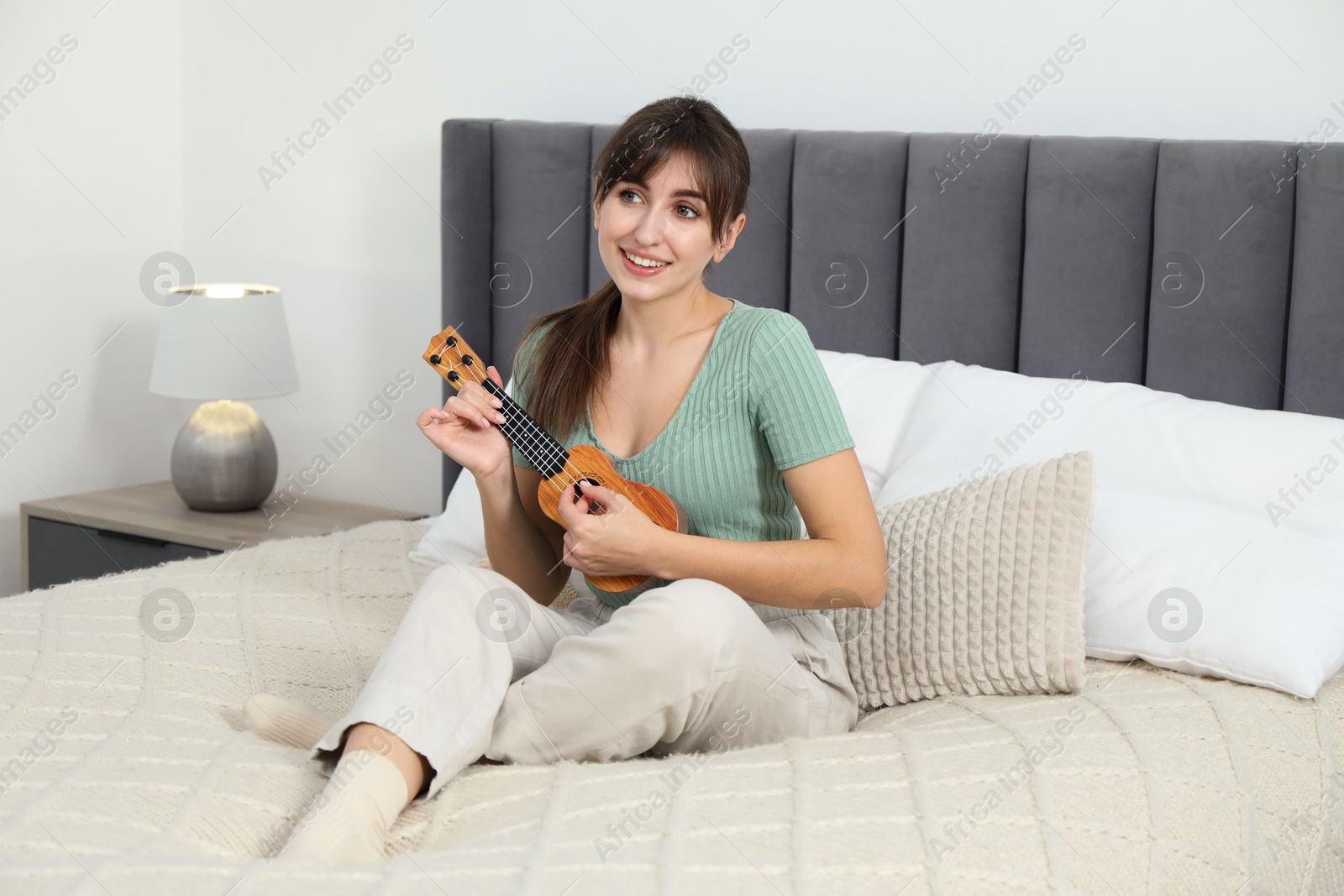 Photo of Happy woman playing ukulele on bed at home