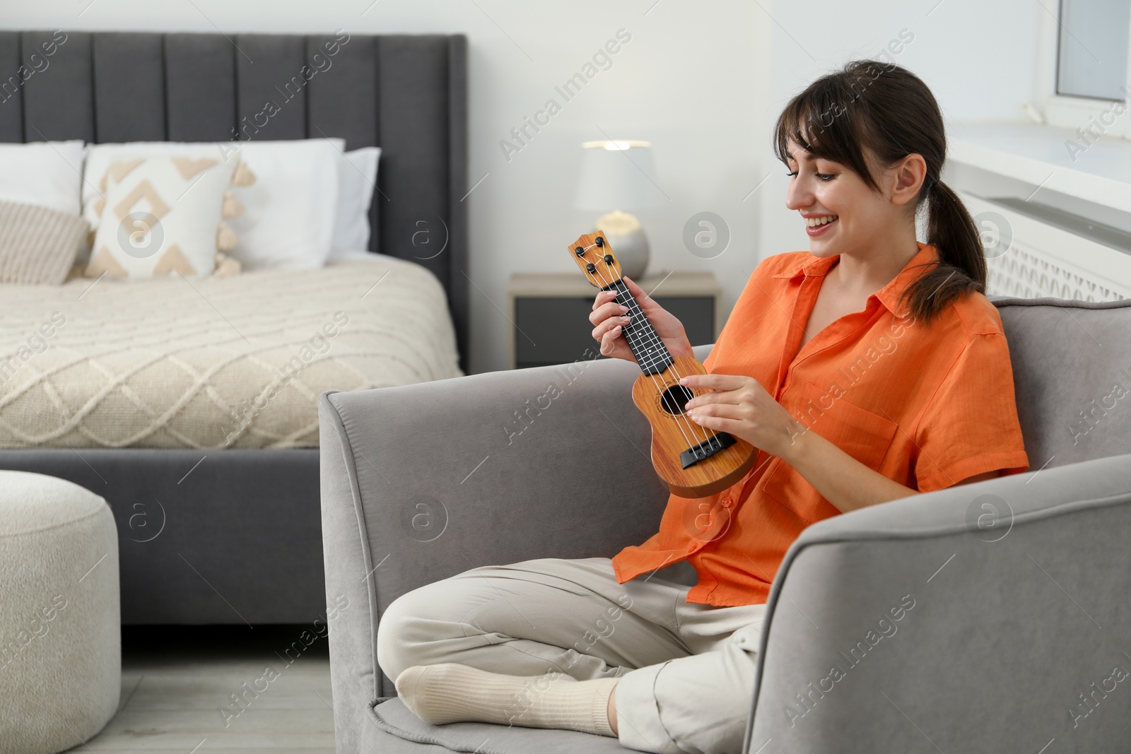 Photo of Happy woman playing ukulele in armchair at home