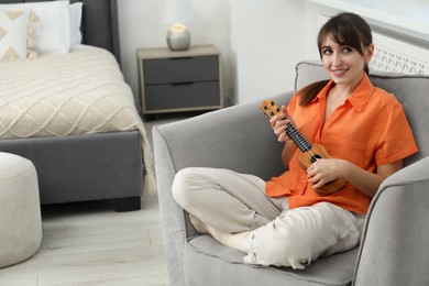 Photo of Happy woman playing ukulele in armchair at home