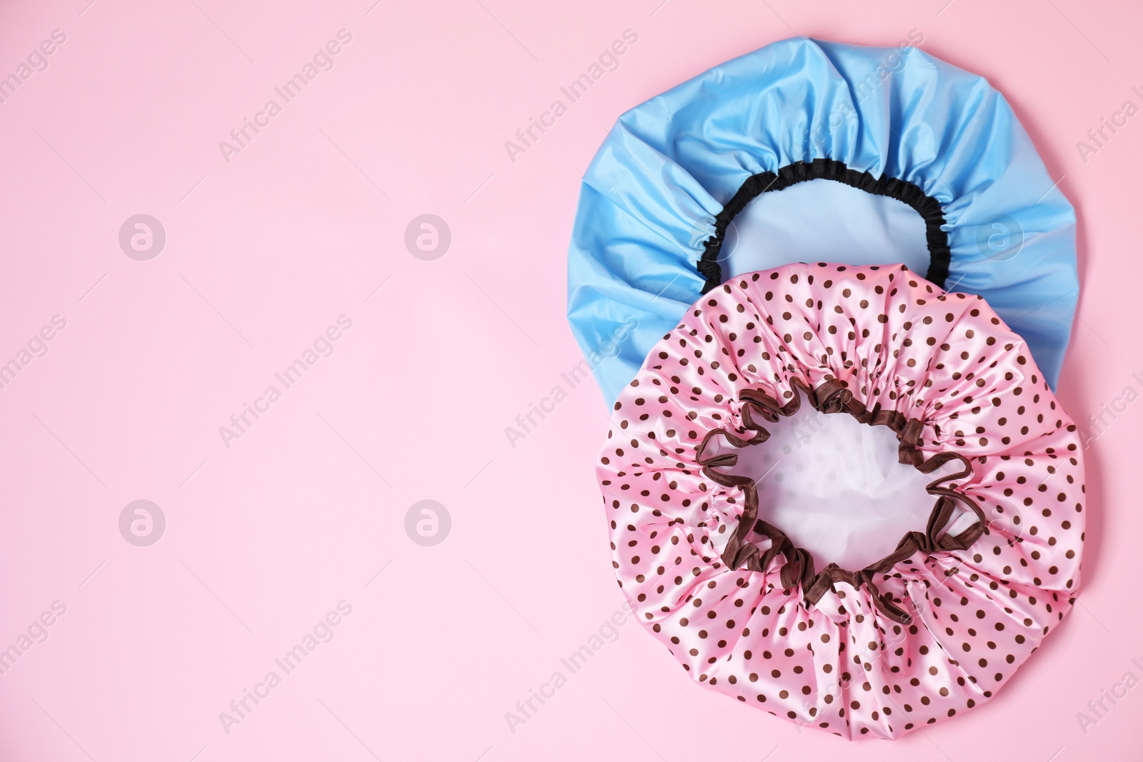 Photo of Two shower caps on pink background, top view. Space for text