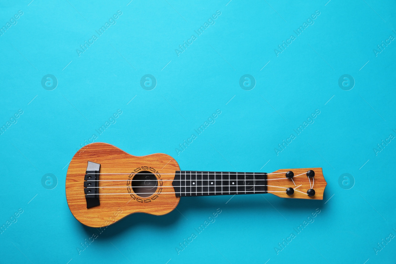 Photo of One ukulele on light blue background, top view. Space for text