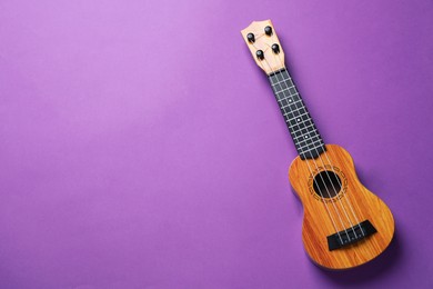 Photo of One ukulele on purple background, top view. Space for text