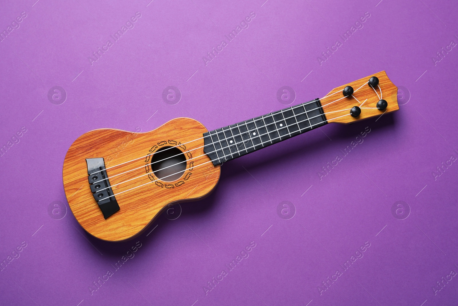 Photo of One ukulele on purple background, top view