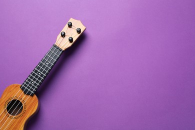 Photo of One ukulele on purple background, top view. Space for text