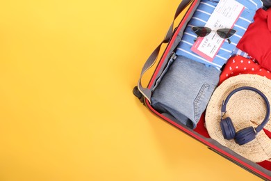 Photo of Travel abroad. Packed suitcase on yellow background, top view. Space for text