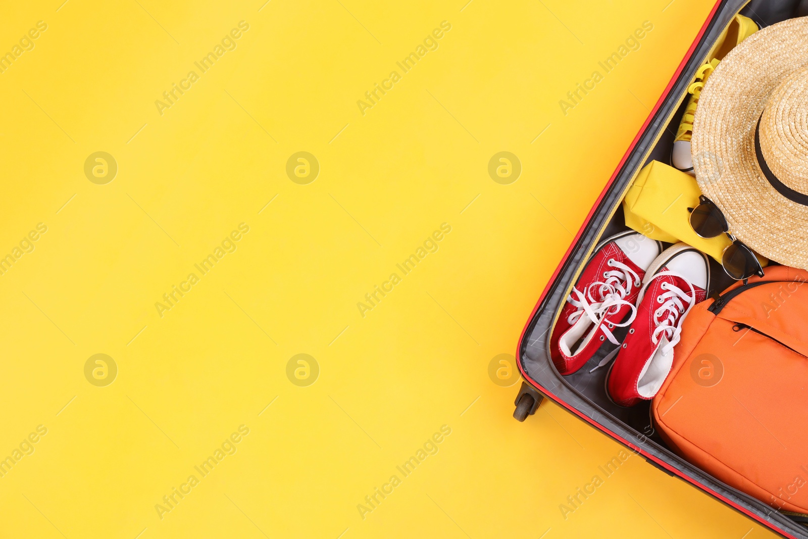 Photo of Travel abroad. Packed suitcase on yellow background, top view. Space for text