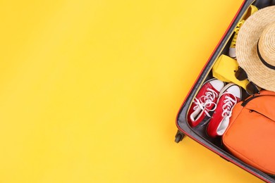 Photo of Travel abroad. Packed suitcase on yellow background, top view. Space for text