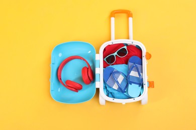 Photo of Travel abroad. Packed mini suitcase on yellow background, top view