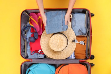 Photo of Traveler packing suitcase on yellow background, top view