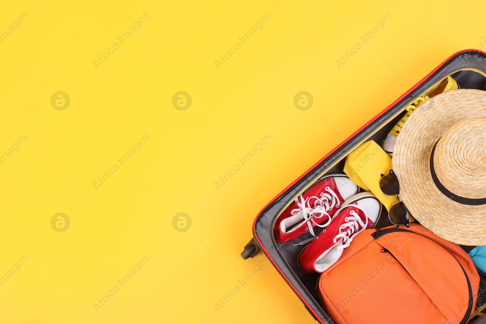 Photo of Travel abroad. Packed suitcase on yellow background, top view. Space for text