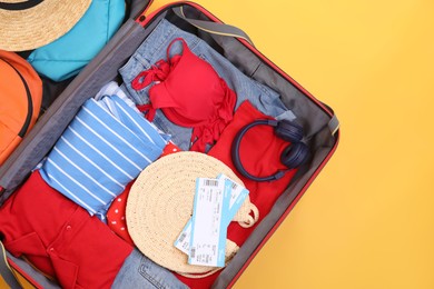 Photo of Travel abroad. Packed suitcase with tickets on yellow background, top view