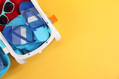 Photo of Travel abroad. Packed mini suitcase on yellow background, top view. Space for text