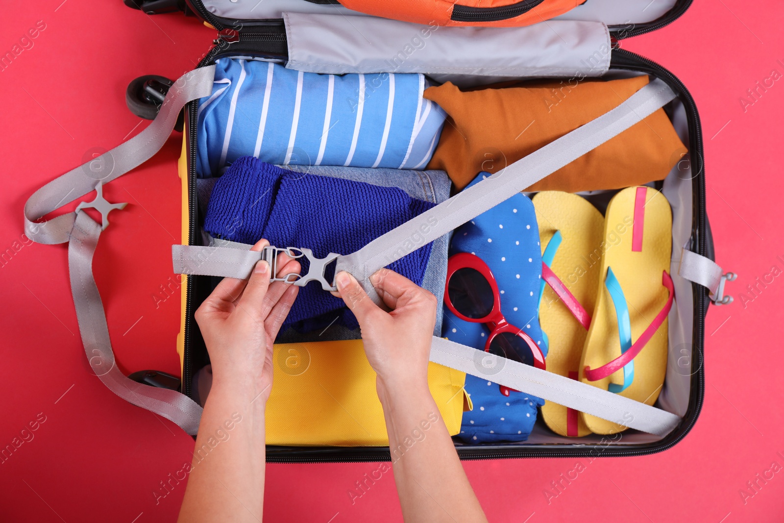 Photo of Traveler packing suitcase on red background, top view